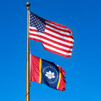 Two flags, one American and one with a blue background and emblem, waving against a clear blue sky.