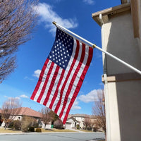 American flag waving in front of a house with a clear blue sky.