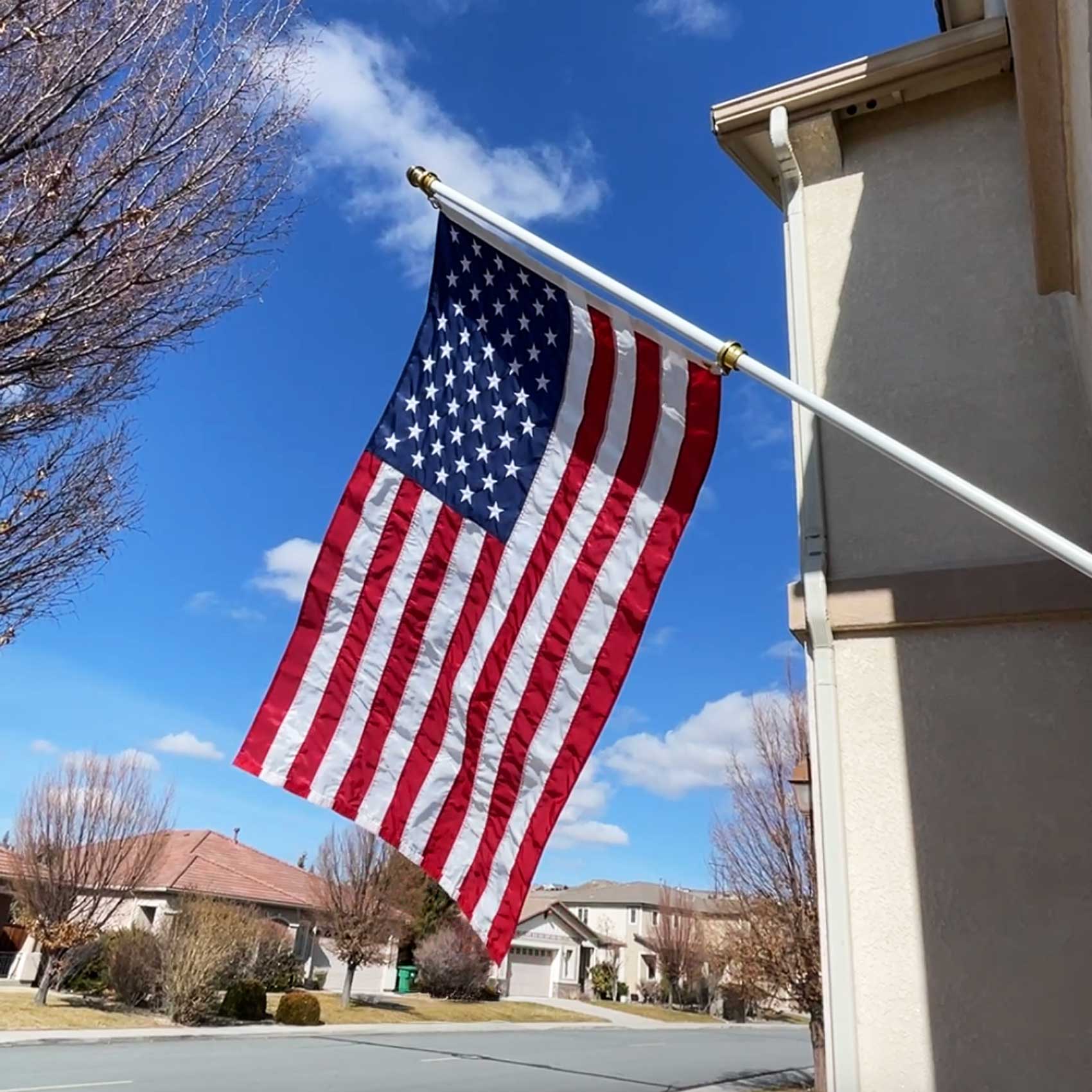 American flag waving in front of a house with a clear blue sky.